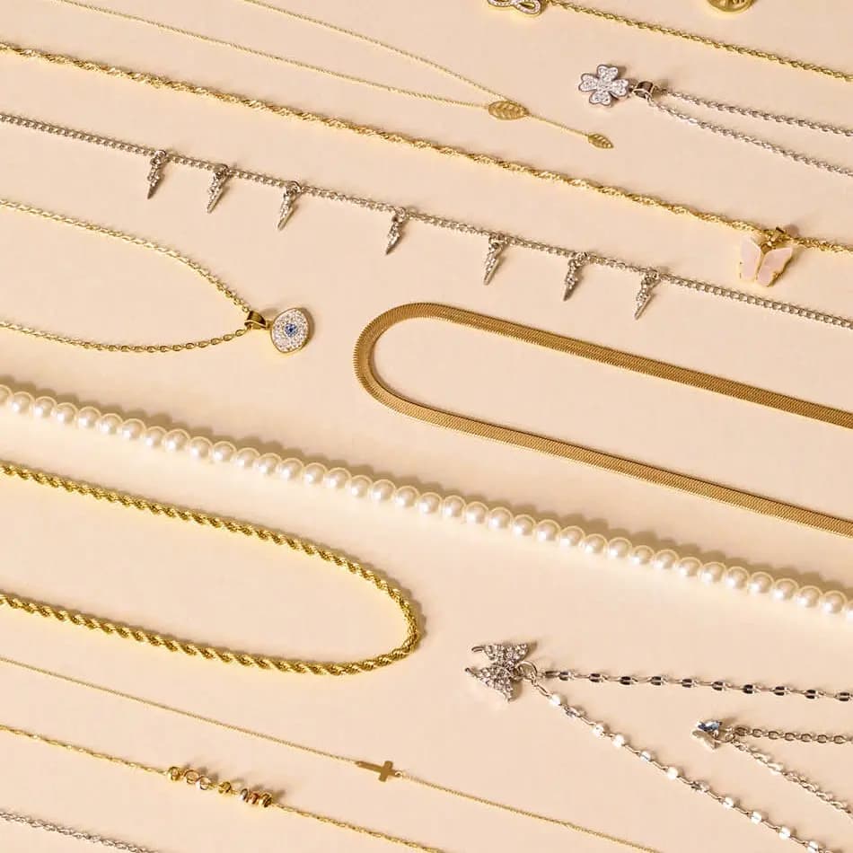 Flera halsband i guld, silver och pärlor mot beige bakgrund